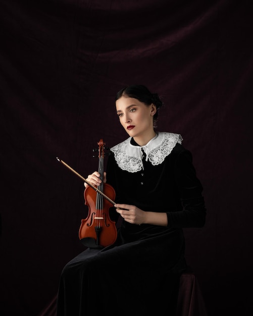 Retrato de estudio hermosa chica con un vestido negro con una viola en sus manos sobre un fondo oscuro