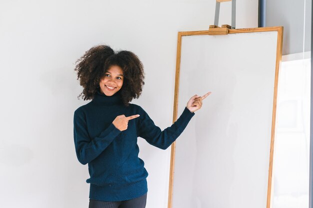 Retrato de estudio de una hermosa joven afroamericana sonriendo a la cámara apuntando con el dedo a la pizarra