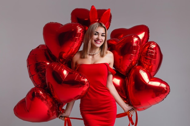 Retrato de estudio de una hermosa niña sonriente en un vestido rojo Modelo posando con globos en forma de corazón