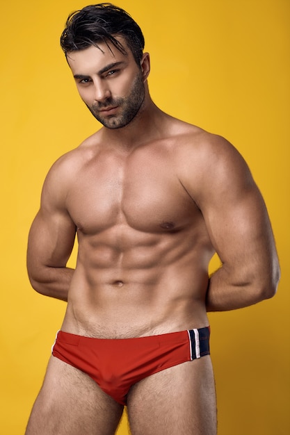 Retrato de estudio de un hermoso hombre musculoso bronceado brutal que llevaba una ropa interior roja sobre un amarillo