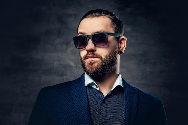 Retrato de estudio de hombre barbudo con gafas de sol y piercing en la nariz.