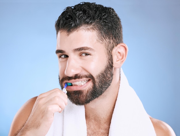 Retrato de estudio hombre y cepillo de dientes para el bienestar dental de los dientes y una sonrisa saludable boca y limpieza Modelo masculino feliz cuidado bucal y aliento fresco para las encías odontología e higiene sobre fondo azul