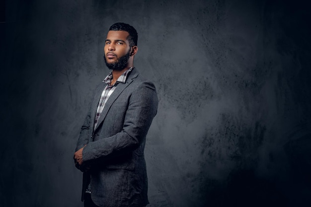 Retrato de estudio de un hombre hipster negro vestido con una camisa de lana y una chaqueta posando sobre un fondo artístico gris.