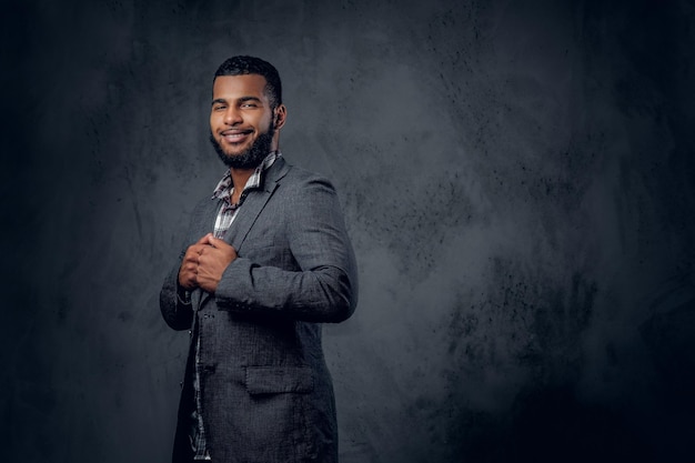 Retrato de estudio de un hombre hipster negro vestido con una camisa de lana y una chaqueta posando sobre un fondo artístico gris.