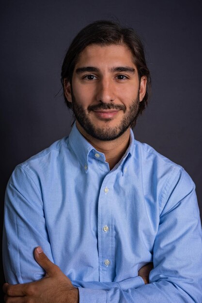 Foto retrato de estudio de un hombre hispano con barba y cabello largo en camisa azul mirando a la cámara