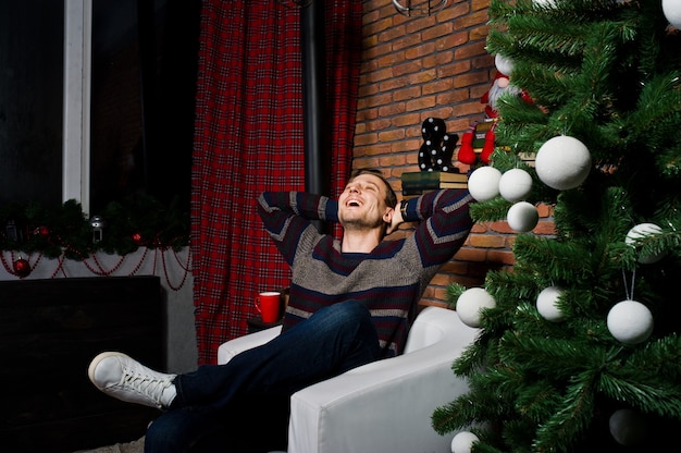 Retrato de estudio de hombre de risas contra el árbol de navidad con adornos.