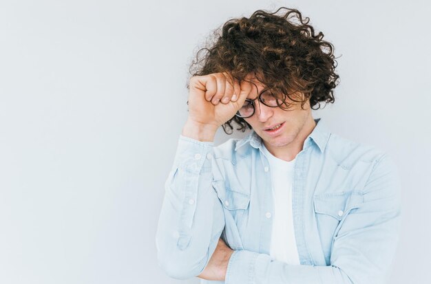 Foto retrato de estudio horizontal de hombre en camisa de mezclilla tiene dolor de cabeza con la mano en la frente mirando hacia abajo después de trabajar en exceso aislado sobre fondo de pared blanca con espacio de copia concepto de emoción de salud de la gente