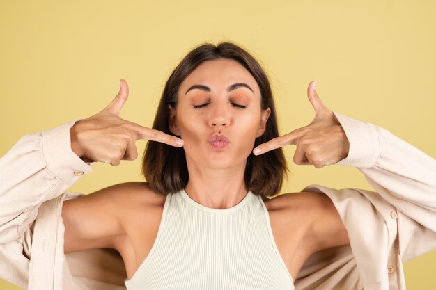 Retrato de estudio interior de mujer feliz con top blanco y camiseta abierta haciendo movimientos tontos en amarillo