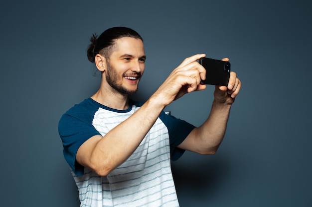 Retrato de estudio de un joven alegre tomando fotos con un smartphone