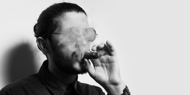 Retrato de estudio de un joven apuesto fumando un cigarro cubano Tema en blanco y negro