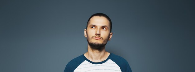 Retrato de estudio de un joven apuesto mirando pensativamente hacia otro lado En el fondo de gris oscuro