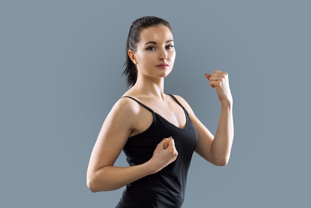 Retrato de estudio de una joven atlética y hermosa mujer con ropa deportiva negra de fondo gris, mujer haciendo ejercicios, cuerpo en poses deportivas