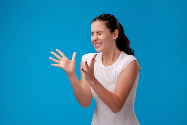 Retrato de estudio de una joven y bella mujer con una camiseta blanca sobre un fondo de pared azul. Personas sinceras emociones.