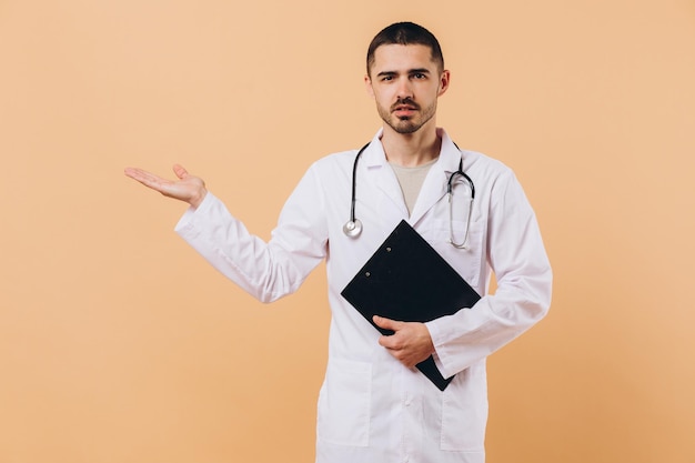 Retrato de estudio de un joven médico masculino con estetoscopio aislado en un espacio de copia beige en el costado