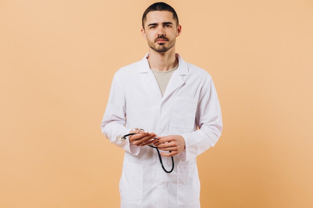 Retrato de estudio de un joven médico masculino con estetoscopio aislado en un espacio de copia beige en el costado