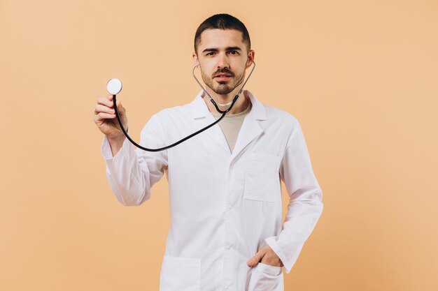 Retrato de estudio de un joven médico masculino con estetoscopio aislado en un espacio de copia beige en el costado