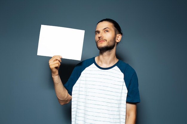 Retrato de estudio de un joven pensativo sosteniendo un tablero de papel blanco vacío en color azul Mirando hacia arriba