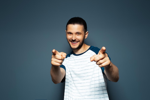 Retrato de estudio de un joven que te señala con el dedo a la cámara en un fondo de color azul