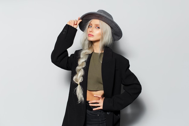 Retrato de estudio de una joven rubia linda con una trenza con abrigo negro y sombrero gris sobre fondo blanco