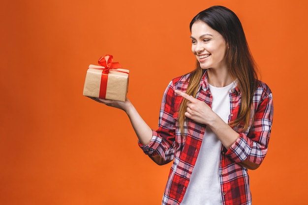 Retrato de estudio de joven sonriente tiene caja de regalo roja. Aislado contra el fondo naranja.