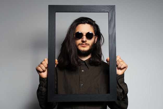 Retrato de estudio de un joven sosteniendo un marco vacío de negro