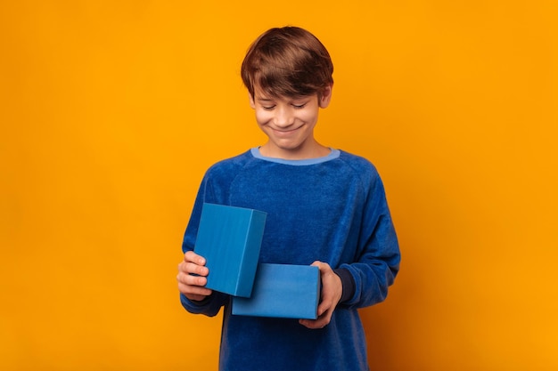 Retrato de estudio de un joven tímido sonriente que abre una caja de regalo azul