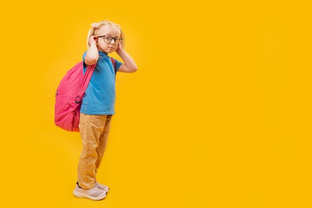 Retrato de estudio de longitud completa con fondo amarillo de una pequeña niña rubia caucásica con mochila para la escuela Espacio de copia