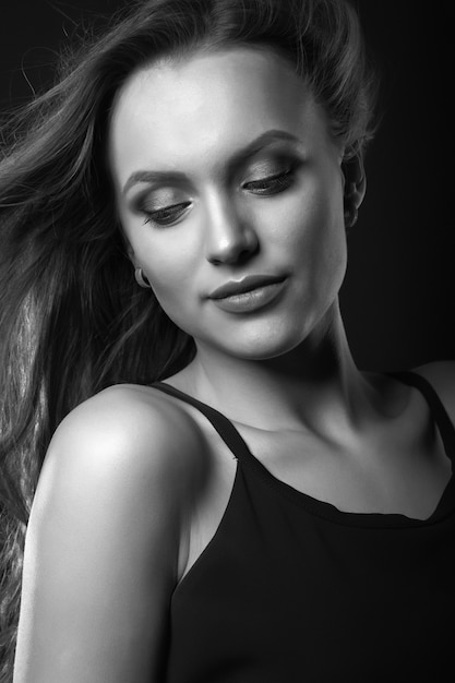 Retrato de estudio de moda de una mujer morena de lujo con maquillaje y peinado perfectos viste un vestido negro clásico posando en un estudio oscuro. Disparo en blanco y negro