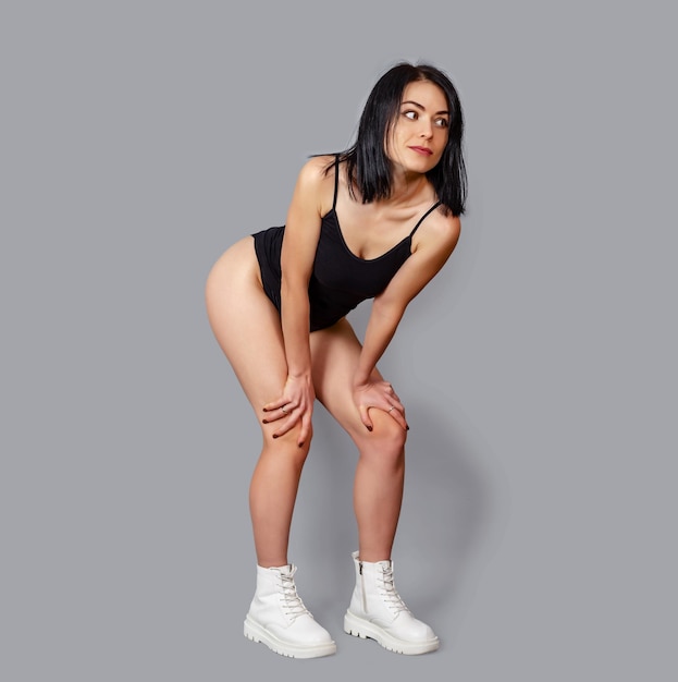 Retrato de estudio de mujer fitness en mono negro zapatillas blancas medio dobladas apoyándose en las rodillas