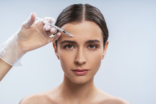 Retrato de estudio de mujer joven y atractiva que llena las inyecciones faciales de belleza en el centro de belleza