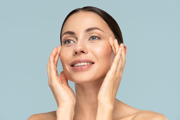 Retrato de estudio de mujer joven con maquillaje natural, cabello peinado, tocando la piel pura bien arreglada