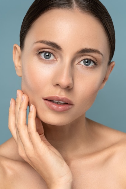 Retrato de estudio de mujer joven con maquillaje natural, cabello peinado, tocando su piel pura bien arreglada