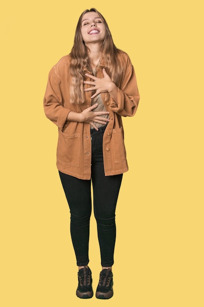 Foto retrato de estudio de una mujer rubia caucásica que ríe felizmente y se divierte manteniendo las manos en el estómago