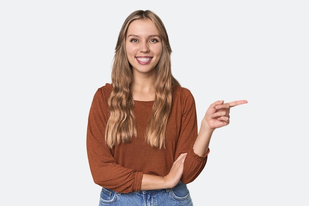 Retrato de estudio de una mujer rubia caucásica sonriendo alegremente señalando con el dedo índice