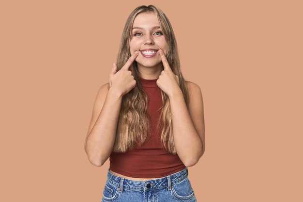 Retrato de estudio de una mujer rubia caucásica sonriendo señalando los dedos a la boca