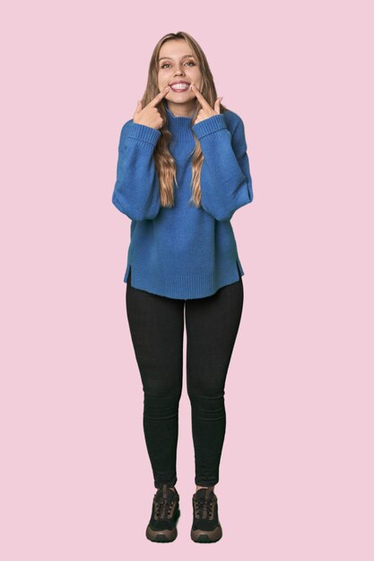 Retrato de estudio de una mujer rubia caucásica sonriendo señalando los dedos a la boca