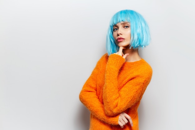 Retrato de estudio de niña bonita con peluca azul y suéter naranja sobre fondo blanco.