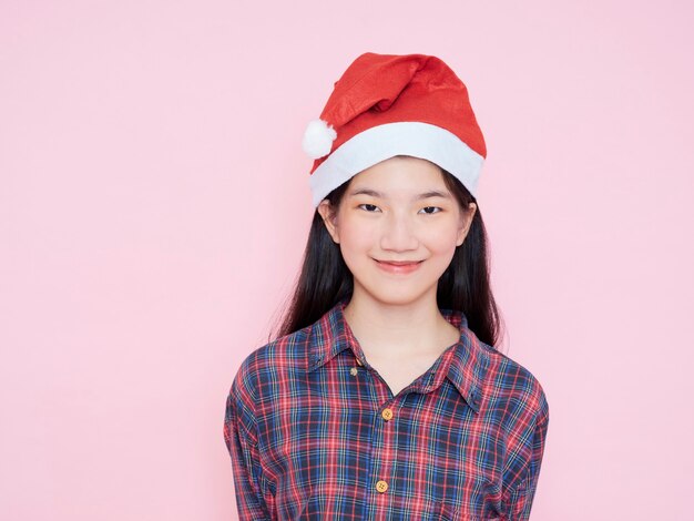 Retrato de estudio de niña con sombrero de santa sobre fondo rosa. Concepto de navidad.