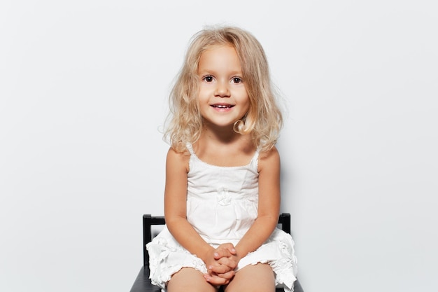 Retrato de estudio de niña sonriente con cabello rubio sobre fondo blanco.