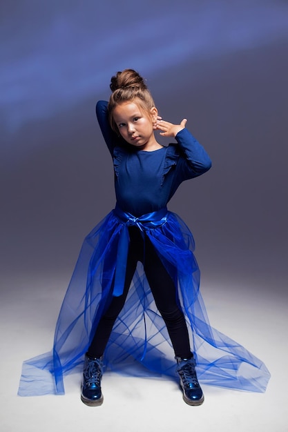 Retrato de estudio de una niña con traje negro y un largo tren azul sobre un fondo oscuro