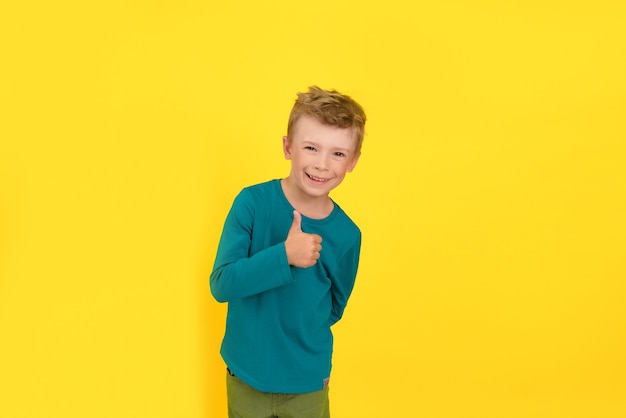 Retrato de estudio de niño feliz mostrando el pulgar hacia arriba gesto, fondo amarillo.