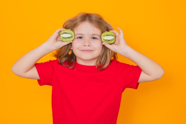 Retrato de estudio de niño lindo niño con kiwi aislado en amarillo