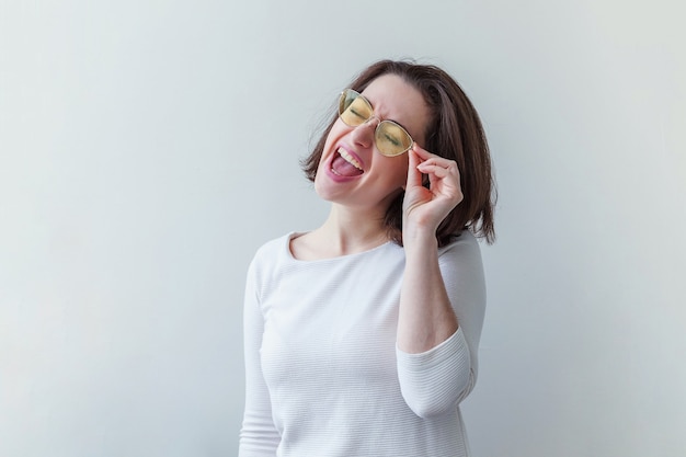 Retrato de estudio simple de moda hipster sonriente chica morena de pelo corto en moda gafas de sol amarillas aisladas en blanco