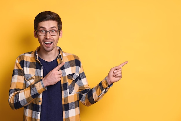 Retrato de estudio de un tipo divertido y feliz con gafas que apunta a un espacio en blanco para el texto