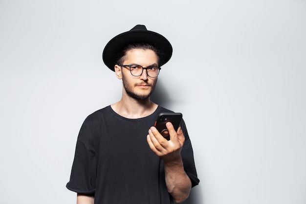 Retrato de estudio de un tipo con sombrero usando un teléfono inteligente en blanco