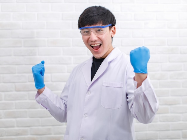 Retrato estúdio tiro cientista masculino profissional asiático em luvas de borracha de jaleco branco em pé sorrindo olhar para a câmera no fundo da parede de tijolo.