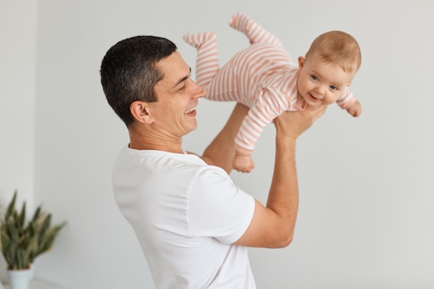 Foto retrato de excitar a un padre adulto joven optimista con su pequeña niña jugando juntos en casa, pretendiendo que un niño volaba como un avión en manos masculinas, expresando felicidad.