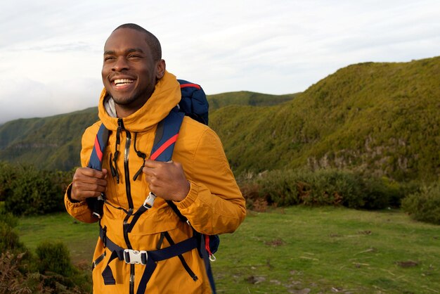 Retrato de un excursionista afroamericano sonriente caminando con mochila en la naturaleza