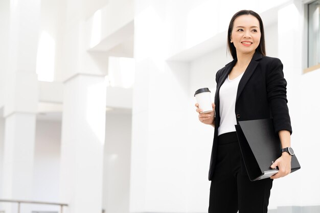 Retrato de una exitosa empresaria asiática de mediana edad sosteniendo café sonriendo a la cámara