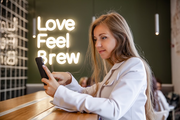 Retrato exitosa empresaria sonriente sentada en la cafetería con smartphone